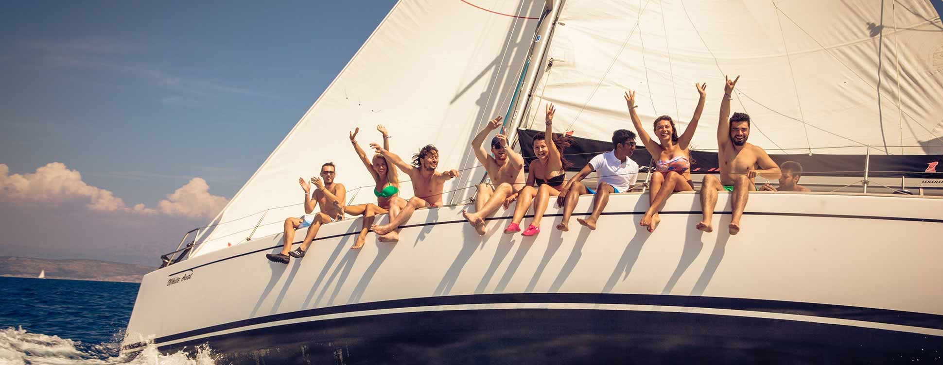mehrere junge Leute sitzten am Rand eines Segelboots und haben gute Laune