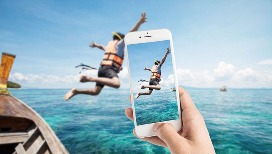 Eine Kind springt von einem Boot ins Wasser und wird dabei mit einem Smartphone fotografiert