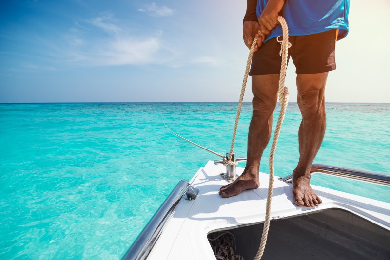 Mann steht mit Seil in der Hand auf einem Boot im flachen Wasser