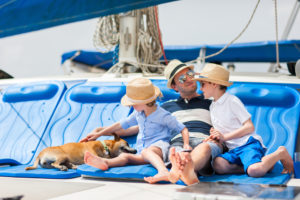 Vater sitzt mit seinen Kindern und Hund auf einem Boot
