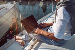 Mann sitzt mit seinem Laptop auf einem Boot und arbeitet