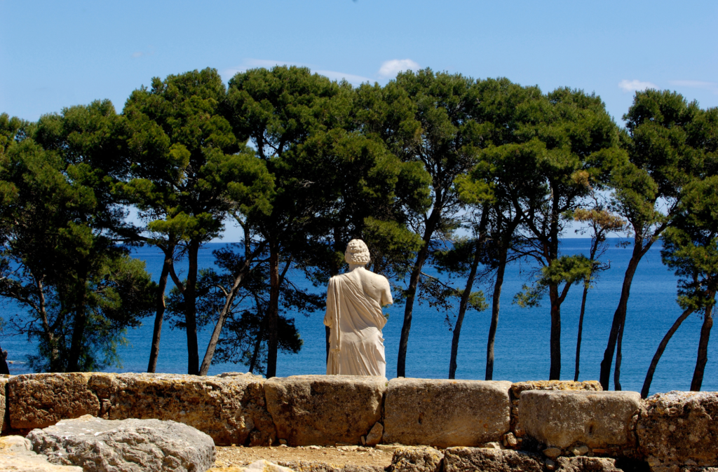 Die Statue des Asklepios von hinten, im Hintergrund das Meer