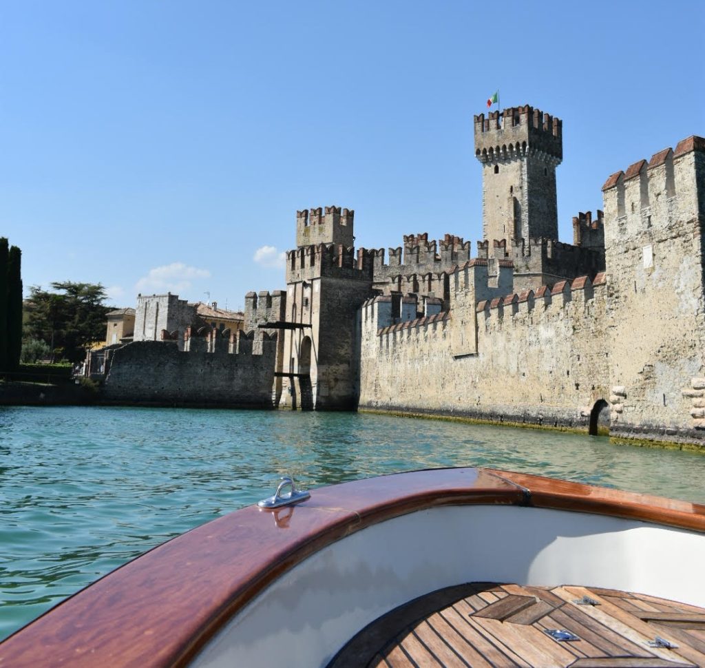 Das Castello di Sirmione vom Boot aus gesehen: eine mittelalterliche Festung im Wasser, im Vordergrund ein Boot.